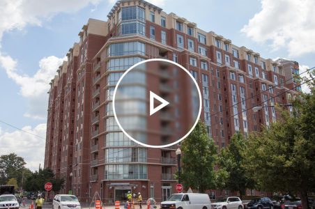Large multifamily building facade during a sunny day with construction and workers directing traffic in front of the building while working.
