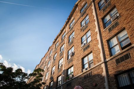 Brick multifamily building facade during the sunset from a sidewalk perspective.