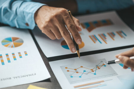 Closeup of a hand pointing to papers with graphs and charts on them.