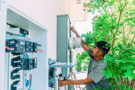 An electrician outside of a home upgrading the electric service panel to 200 amps, also known as a heavy-up.
