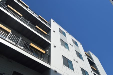 View of a white affordable multifamily building facade from the ground level looking up with a deep blue sky above.