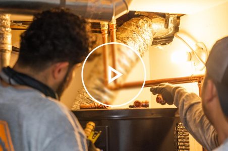 Two HVAC technicians installing a heat pump water heater in a home.