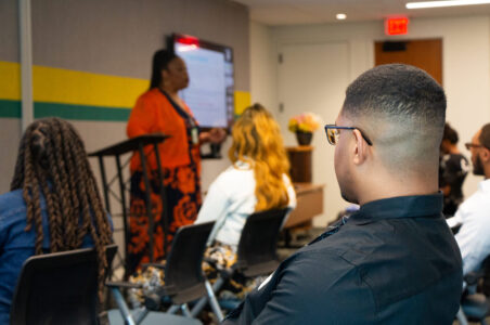 Adult student looking at an instructor while they give a presentation in an office classroom setting.