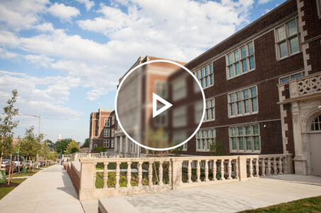 Red brick and stone university building facade on a sunny day with a play button graphic over the image.