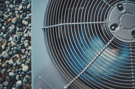 Closeup of the top of a heat pump compressor with the fan blades spinning.