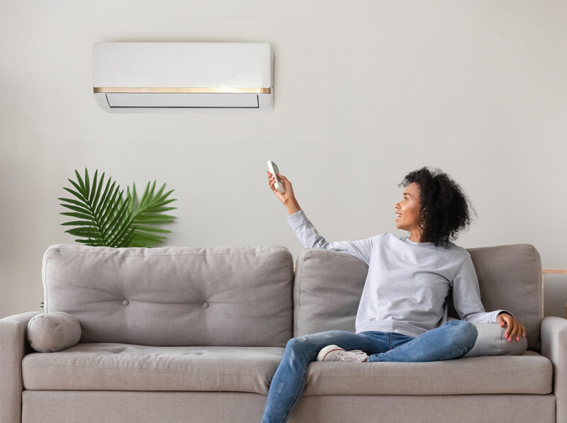 Person sitting on a couch pointing a remote at a mini split heat pump air handler.