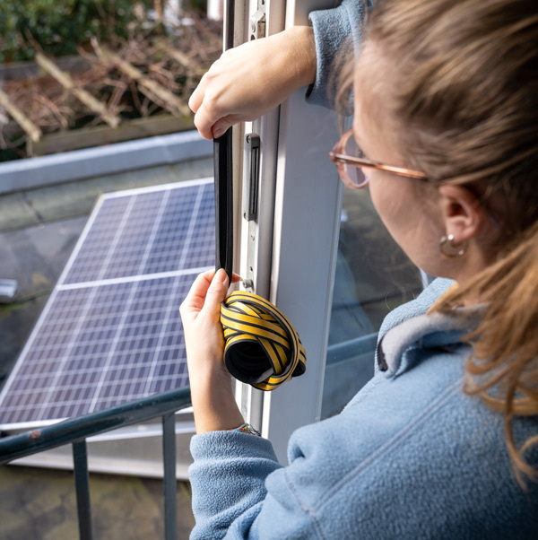 Closeup of a person putting weather strips around a sliding glass door with solar panels visible outside.