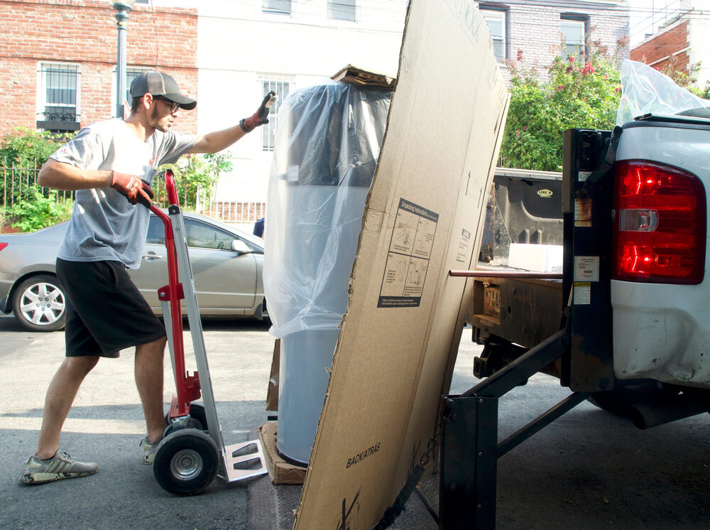 Worker taking a heat pump water heater off of a flatbed pickup truck.