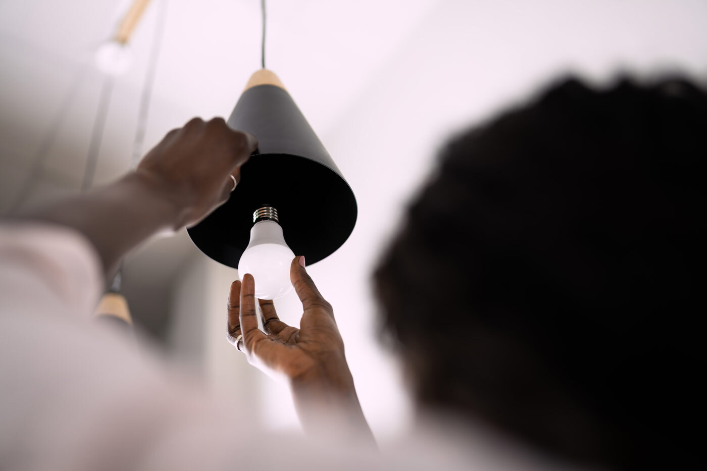 Person screwing in a LED lightbulb into a pendant light fixture.