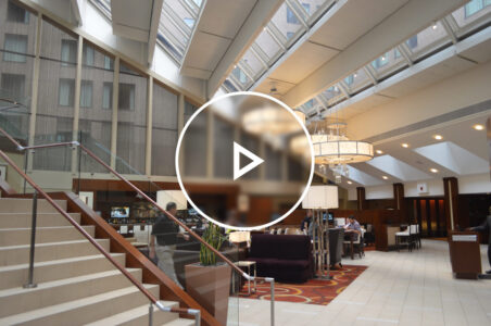 View of the ground floor of a downtown DC hotel with a grand staircase and in-hotel restaurant visible and many patrons moving throughout the space.