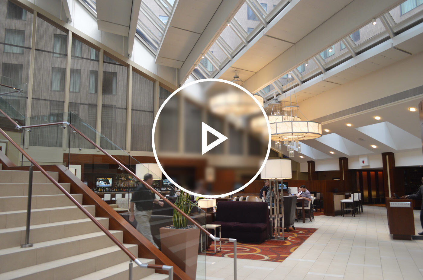 View of the ground floor of a downtown DC hotel with a grand staircase and in-hotel restaurant visible and many patrons moving throughout the space.